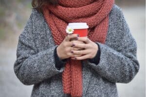 Cozy woman holding hot coffee outdoors during autumn in Diamond Creek Shopping area.