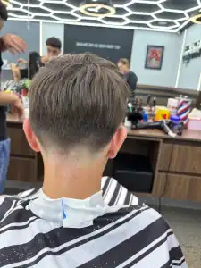 A young man with a modern fade haircut sitting in a barbershop, Clipper Lounge, at Diamond Creek Sho.