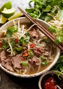 Delicious Vietnamese beef pho with fresh herbs, noodles, and spicy chili peppers.