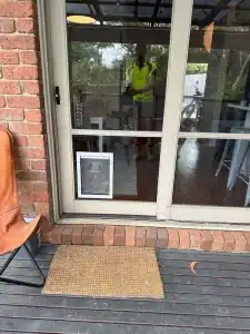 Glass door with reflection of a person in high-visibility vest at Eltham Glass.