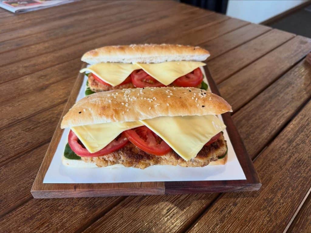 Fresh chicken schnitzel sandwiches with cheese and tomato on a wooden tray at Diamond Creek Shopping.