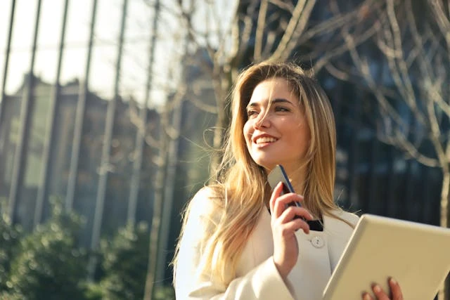 Woman smiling outdoors at Diamond Creek Shopping with tablet in hand.
