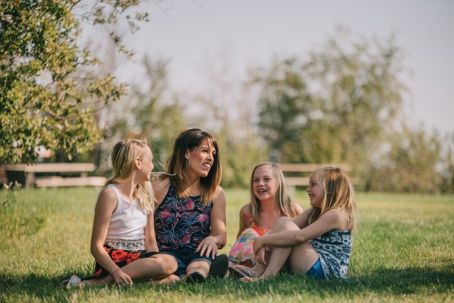 Mother and three girls sitting on grass in a park enjoying sunny day.
