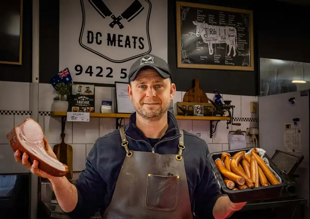Butcher holding a steak and tray of sausages at DC Meats, Diamond Creek.