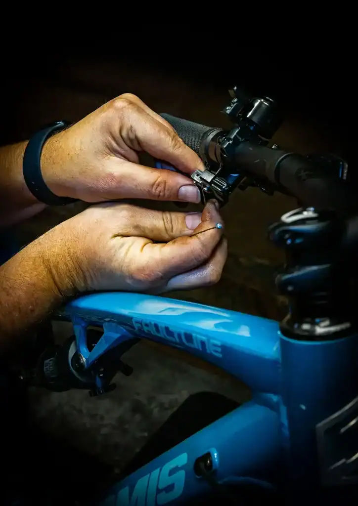 Hands adjusting a bicycle handlebar with a blue frame in a dark setting.