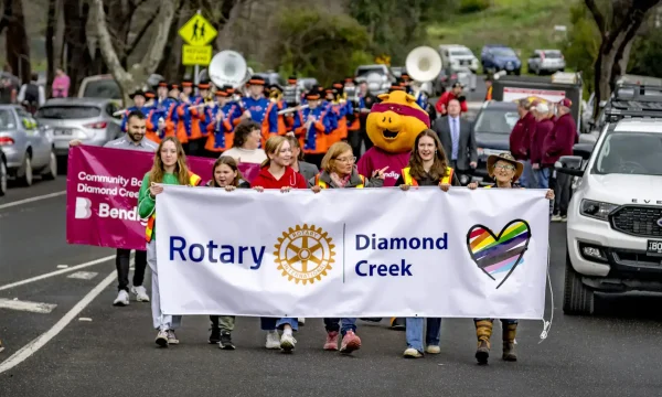 Community parade with Rotary and Diamond Creek banners, mascot, and marching band.