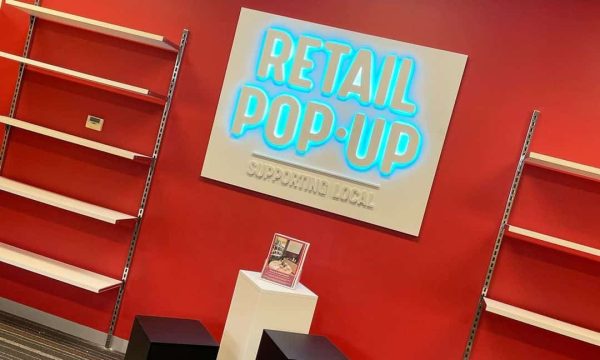 Bright retail pop-up store with empty shelves and neon signage supporting local shopping.