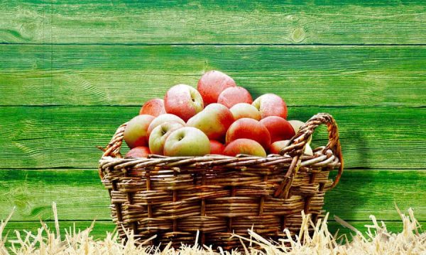 Fresh apples in a wicker basket on a green wooden background.