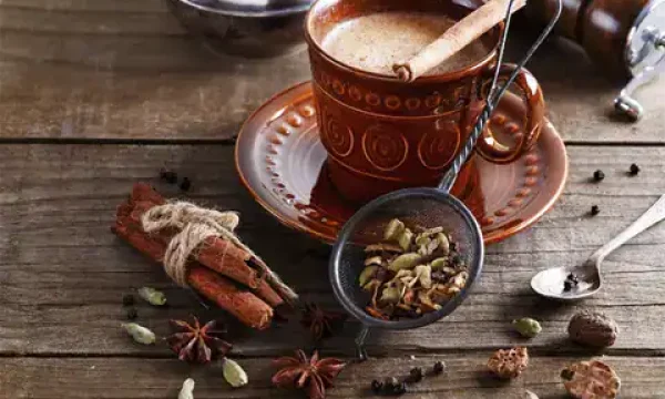 A cup of chai tea with spices, cinnamon, and star anise on a wooden table.