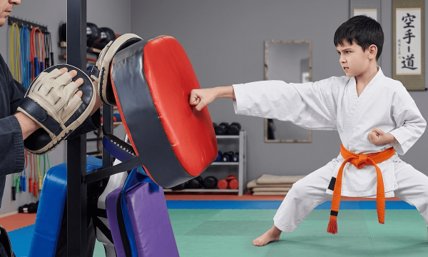 Young boy practicing karate punch with instructor in dojo.
