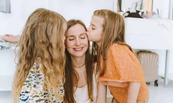 A mother with two young daughters sharing a kiss, celebrating Mother's Day at home.